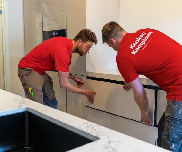 Twee monteurs die een keukenla in beige keuken monteren